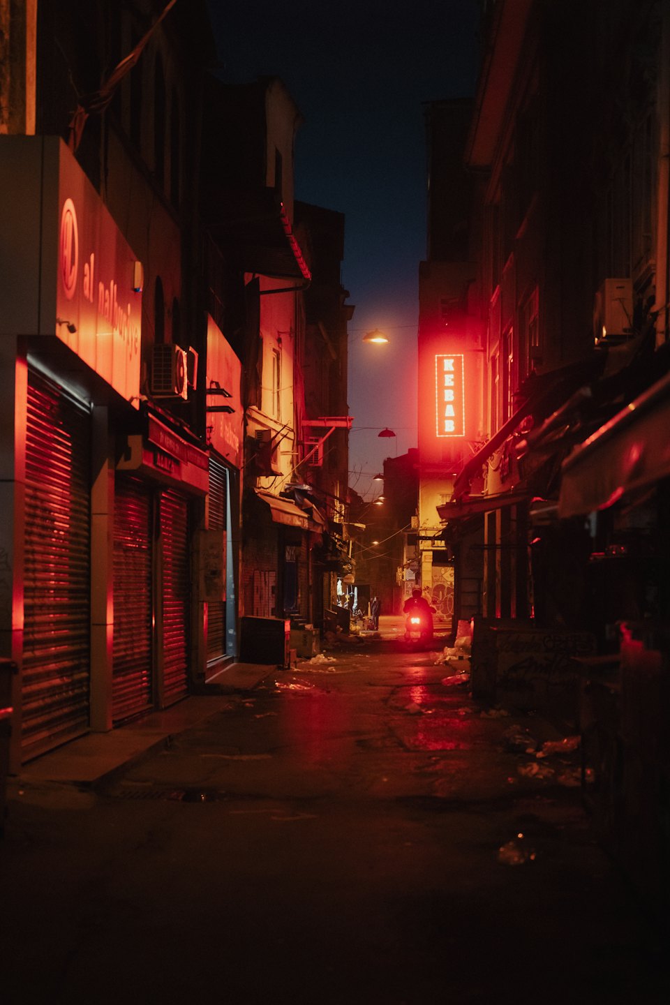 A scooter drives away through a dark urban alleyway.