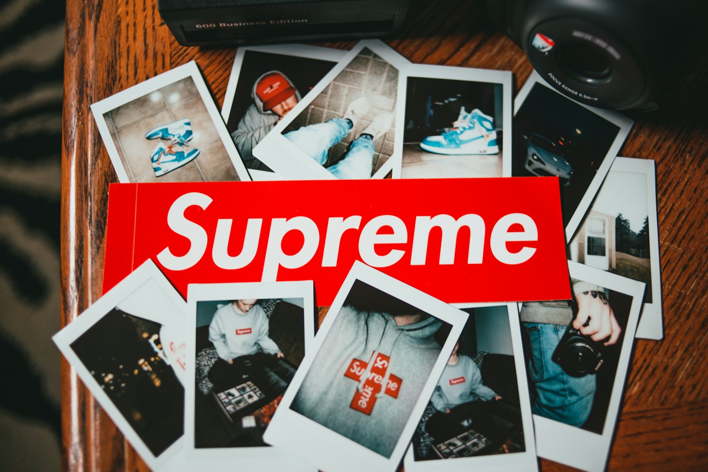 A red sticker surrounded by instant photos on a wooden table.