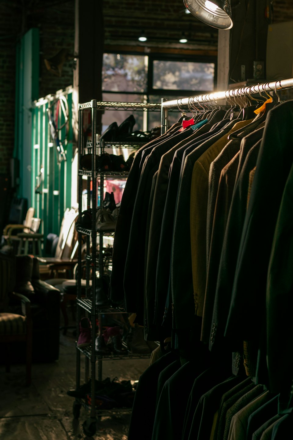 Dark jackets and suits hanging on a rack with shoes on shelves.