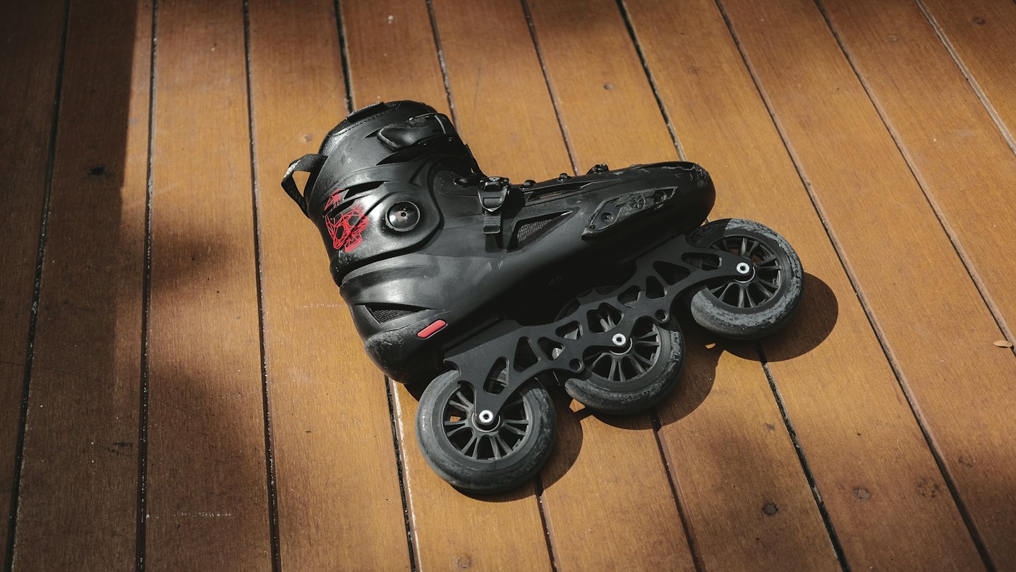 A black inline skate with red details on a wooden deck.